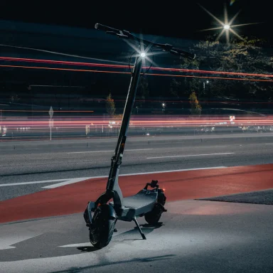 Apollo City electric scooter along a city sidewalk, with modern buildings and street furniture softly blurred in the background.
